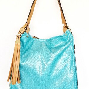 May include: A bright turquoise hobo bag featuring a textured snakeskin-like pattern, a single tan shoulder strap, and a long tan tassel accent attached to a gold-toned metal ring on the side. The bag has a slouchy silhouette and gold hardware.