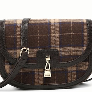 May include: A brown plaid crossbody bag with a flap closure. The bag features a dark brown leather trim, a matching adjustable strap, and gold-tone hardware. The bag is approximately 10 inches wide.