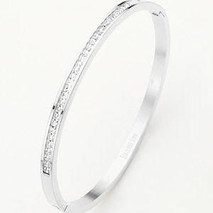 May include: A silver bangle bracelet with a row of clear cubic zirconia stones around the band. The bracelet is engraved with "Stainless Steel".