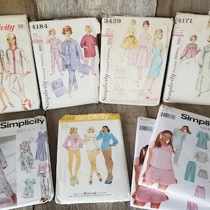May include: A collection of vintage Simplicity sewing patterns for clothing. The patterns are for pajamas, dresses, and tops. The patterns are in various colors and designs.