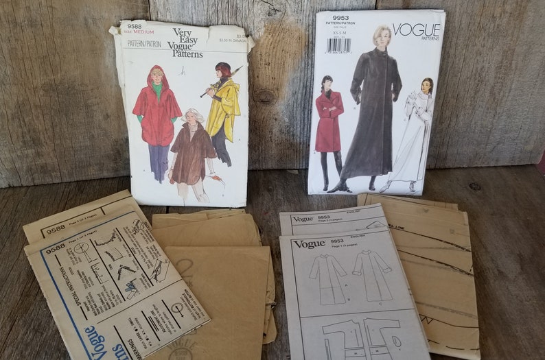 May include: Three vintage Vogue sewing patterns for coats. The patterns are for sizes 8-18. The patterns are on a wooden surface.