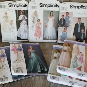 May include: A collection of Simplicity sewing patterns for dresses. The patterns feature various styles, including a long white dress, a pink dress, a blue dress, and a pink and white dress. The patterns are all in different sizes and are all in good condition.