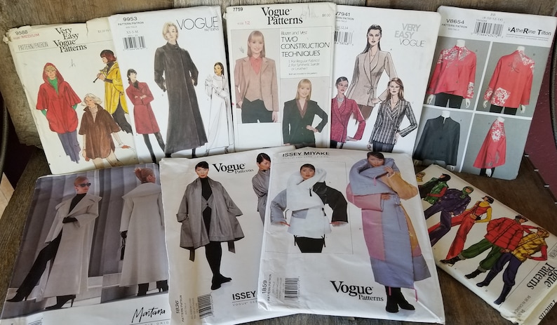 May include: A collection of sewing patterns for coats and jackets. The patterns are from Vogue and Issey Miyake. The patterns feature different styles, including a long black coat, a white coat with a fur collar, and a red jacket with a floral design.