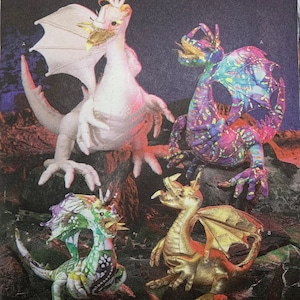 May include: Simplicity pattern 4063 featuring four dragon figures in various colors. The dragons have wings, horns, and detailed features. The pattern includes the text "ONE SIZE" and the Simplicity logo.