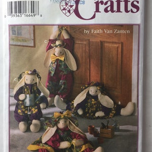 May include: Simplicity Crafts pattern featuring bunny dolls in various poses. The bunnies wear outfits with floral patterns, including dresses, hats, and bow ties. The pattern cover includes the text "Simplicity Crafts" and "by Faith Van Zanten."