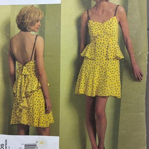 May include: A yellow Anna Sui Vogue dress pattern. The dress features a sweetheart neckline, thin straps, and a peplum waist. The fabric is patterned with small dark shapes. The back of the dress has a low cut and a bow detail. The pattern number is V1105.