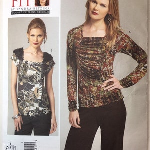 May include: Vogue Patterns original sewing pattern V1275. The pattern features two tops with square necklines. One top has short sleeves with a ruffled trim, and the other has long sleeves. The tops have a floral pattern.