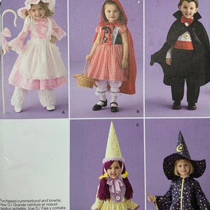 May include: Simplicity pattern 2571 features children's costume designs. The image shows a Little Bo-Peep, Little Red Riding Hood, a vampire, a fairy, and a witch. The costumes include dresses, capes, hats, and accessories. The pattern size is A 1/2, 1, 2, 3, 4.