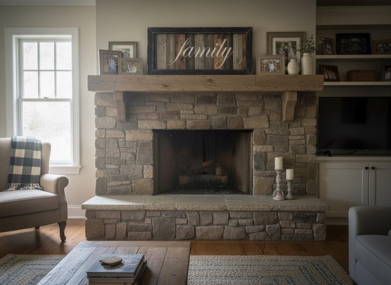 May include: A stone fireplace with a wooden mantel and a framed sign that says "family". The fireplace has a large opening and is flanked by a window and a built-in cabinet with a television. There are framed photos and candles on the mantel.