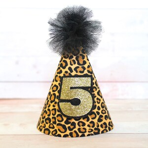 May include: A leopard print party hat with a black tulle pom-pom on top. The hat has a gold glitter number "5" on the front.