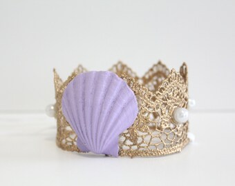 May include: A gold crown with a purple seashell and white pearl accents. The crown is made of lace and has a delicate design.