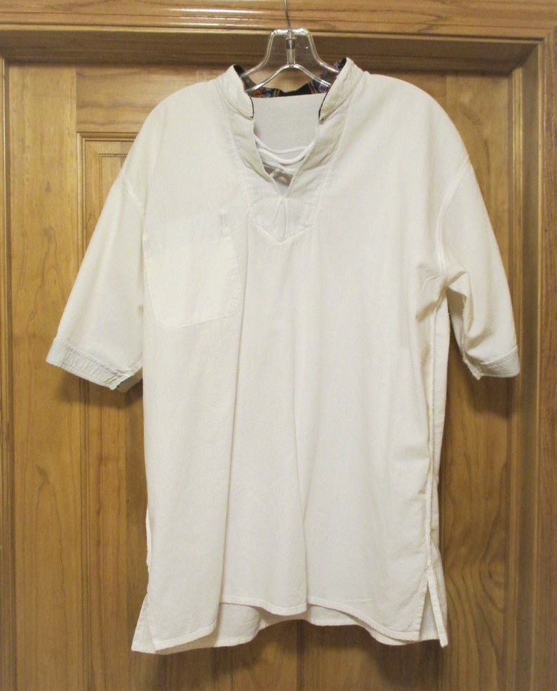 May include: A white, short-sleeved shirt with a lace-up neckline and a single pocket on the left side. The shirt has a longer length in the front and back, and the sleeves have a blue and white striped trim.