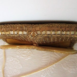 May include: A gold beaded clutch purse with a rectangular shape and a long, thin strap. The purse is covered in small, shiny gold beads, giving it a textured appearance. The purse is likely vintage.