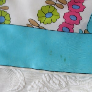 May include: A turquoise blue fabric with a white border and a floral pattern in shades of pink, green, and blue.
