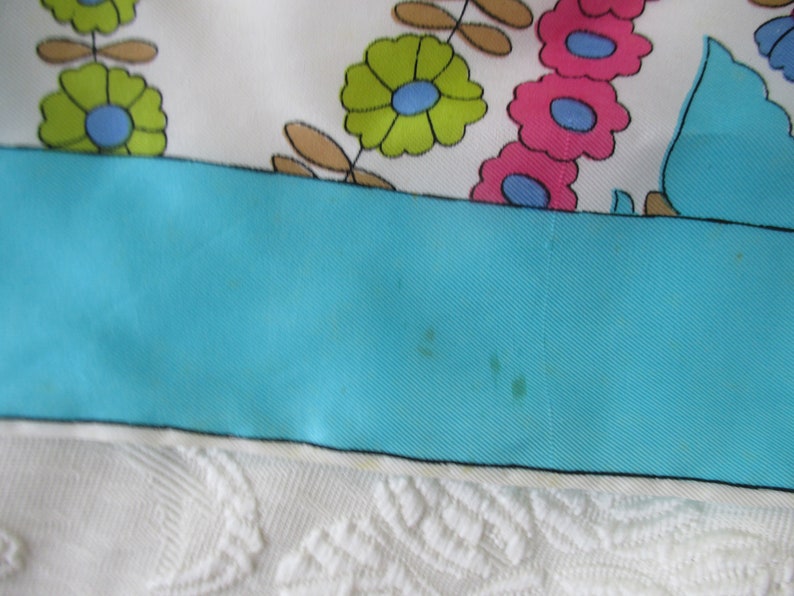 May include: A turquoise blue fabric with a white border and a floral pattern in shades of pink, green, and blue.