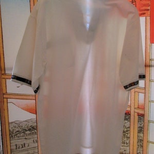 May include: White short-sleeved collared shirt with a black and multi-colored patterned collar.