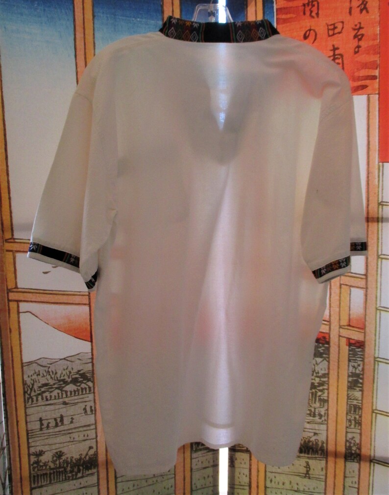 May include: White short-sleeved collared shirt with a black and multi-colored patterned collar.