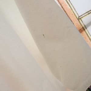 May include: A white fabric tablecloth with a slight brown stain. The tablecloth is folded in half and the edge of the fabric is visible.