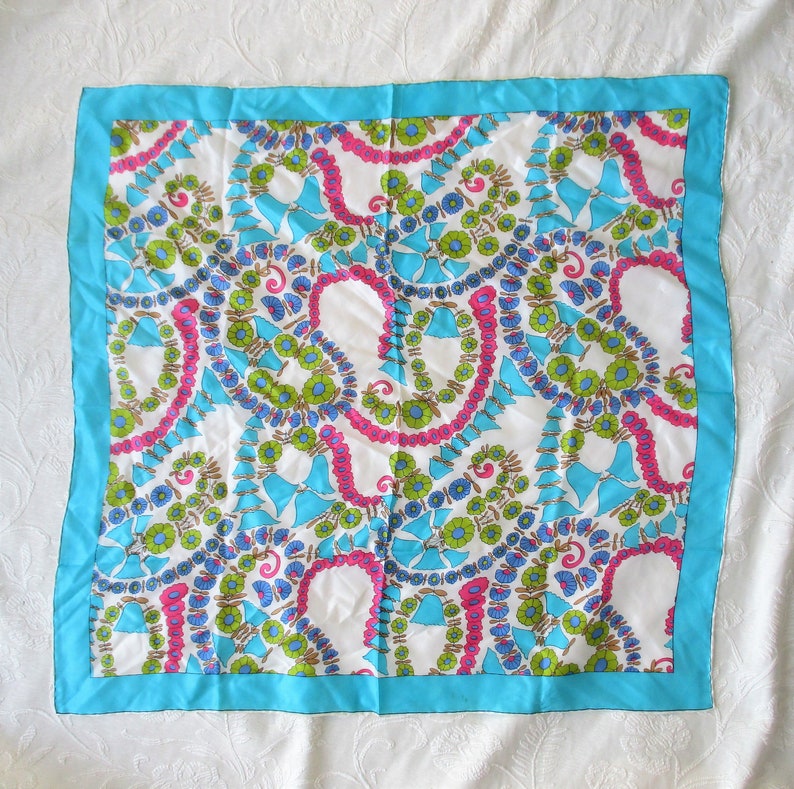 May include: A white silk scarf with a blue border and a colourful paisley pattern. The pattern features pink, blue, green, and brown colours.