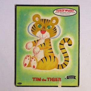 Puede incluir: Un rompecabezas de imagen flocado vintage con un tigre de dibujos animados llamado Tim. El rompecabezas se titula "Tim the Tiger" y forma parte de la línea de rompecabezas preescolares "Fuzzy Wuzzzy".