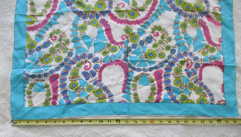 May include: A white silk scarf with a blue, green and pink floral pattern. The scarf has a turquoise border.