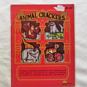 May include: A vintage coloring book titled "Animal Crackers" with a red cover and illustrations of animals in cages. The book features a price tag of $6.50 and the text "All types of animals illustrated in color with black and white patterns. Instructions for method of painting all. Written by nationally known artist Jan McCraw."