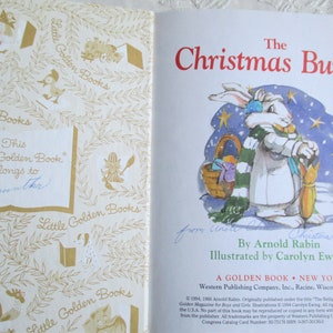 May include: A vintage Little Golden Book titled "The Christmas Bunny" by Arnold Rabin, illustrated by Carolyn Ewing. The cover features a white bunny wearing a green and white scarf, holding an umbrella, and standing in a snowy landscape with stars.