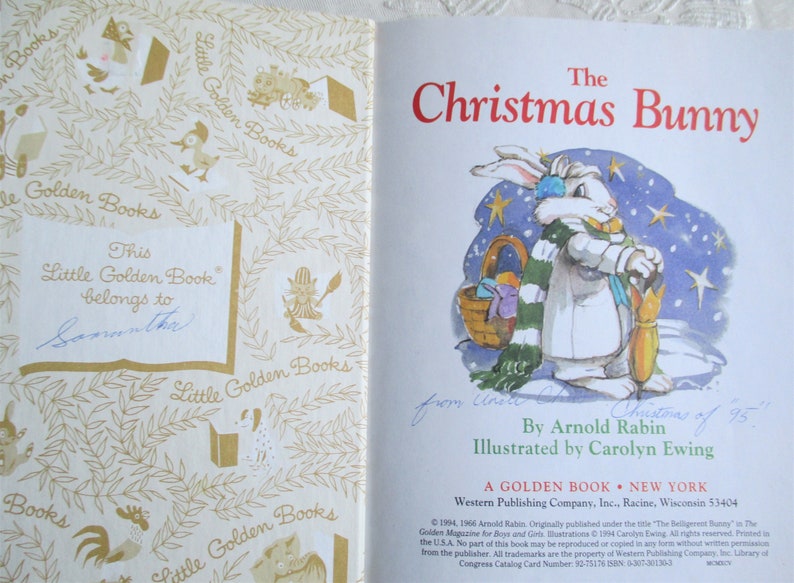 May include: A vintage Little Golden Book titled "The Christmas Bunny" by Arnold Rabin, illustrated by Carolyn Ewing. The cover features a white bunny wearing a green and white scarf, holding an umbrella, and standing in a snowy landscape with stars.