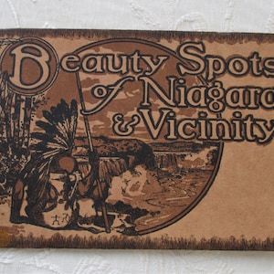 May include: A vintage postcard with a brown background and a black border. The text "Beauty Spots of Niagara & Vicinity" is printed in a decorative font. The image features a black and white illustration of a Native American figure and a waterfall.
