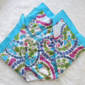 May include: A white silk scarf with a blue, green and pink floral pattern. The scarf has a turquoise border.