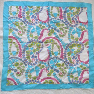 May include: A white silk scarf with a blue, pink and green floral pattern. The scarf has a turquoise border.