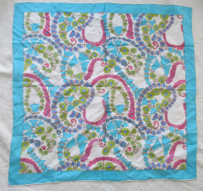 May include: A white silk scarf with a blue, pink and green floral pattern. The scarf has a turquoise border.