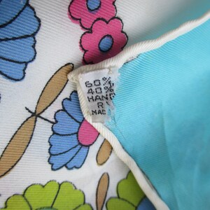 May include: Close-up of a white fabric with a blue, pink and green floral pattern. The fabric has a tag attached that reads "60% 40% HAND R MADE".