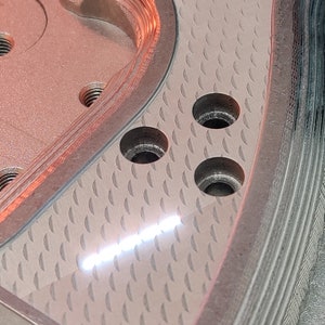 K&ouml;nnte beinhalten: Ein silberner Metallgriff f&uuml;r eine Pistole mit einer strukturierten Oberfl&auml;che und drei L&ouml;chern. Der Griff hat ein gerilltes Design an der Seite.