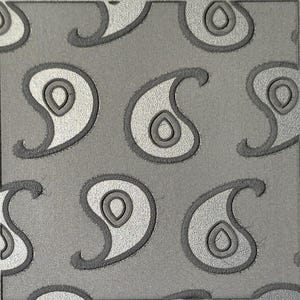 May include: A square material swatch featuring a repeating dark gray paisley pattern embossed onto a lighter gray background. The teardrop-shaped motifs are outlined with a raised texture, creating a distinct contrast between the two shades of gray.