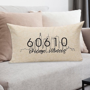 May include: A beige throw pillow with a black outline of the Chicago skyline and the text "60610 Chicago, Illinois".