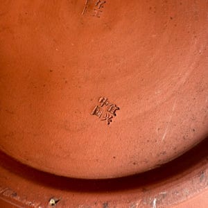 May include: Close-up of a terracotta-colored ceramic object with Chinese characters stamped on the surface. The object has a slightly textured appearance and a warm, earthy tone.