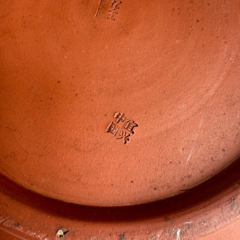 May include: Close-up of a terracotta-colored ceramic object with Chinese characters stamped on the surface. The object has a slightly textured appearance and a warm, earthy tone.