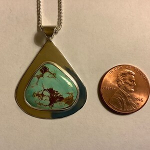 May include: A silver pendant with a turquoise stone set in a teardrop shape. The pendant is about the size of a US penny.