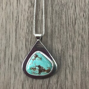 May include: A silver pendant necklace with a turquoise stone set in a teardrop-shaped frame.
