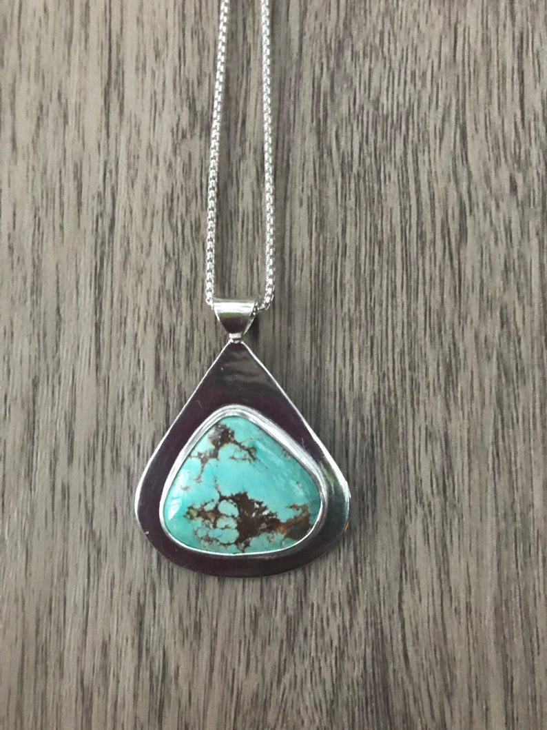 May include: A silver pendant necklace with a turquoise stone set in a teardrop-shaped frame.