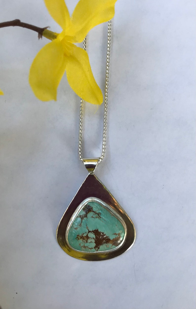 May include: A silver chain necklace with a teardrop-shaped pendant featuring a turquoise stone with brown markings.