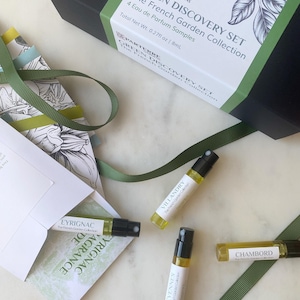 May include: A black gift box with a green band and the text "Green Discovery Set The French Garden Collection". Four perfume samples and a green ribbon are arranged on a marble surface.