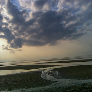 May include: A cloudy sky over a vast, sandy beach with a shallow, rippling stream of water flowing through the sand.