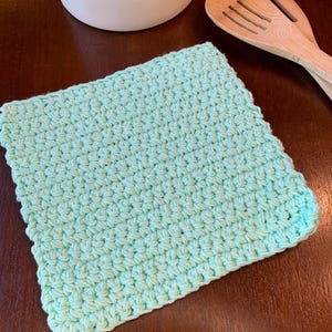 May include: A light green crocheted kitchen dishcloth or pot holder. The dishcloth is made with a simple stitch pattern and has a square shape.