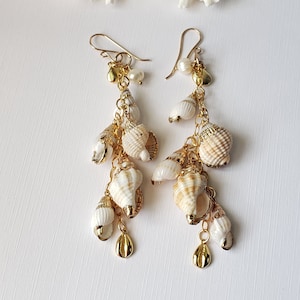May include: Gold tone dangle earrings with multiple white seashells and gold accents.