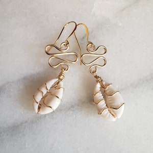 May include: Gold wire earrings with a white seashell charm. The wire is twisted into a decorative design.