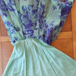 May include: A mint green dress with a sheer overlay featuring a purple floral pattern. The dress has a gathered waist and a flowing skirt, creating a soft, feminine silhouette. The fabric appears lightweight and suitable for warm weather.