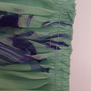 May include: Close-up of a mint green dress with a floral pattern in shades of purple and blue. The fabric is sheer and gathered, creating a textured effect. The dress appears to be made of a lightweight material.
