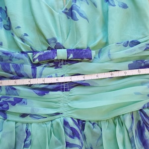 May include: A light green dress with a blue floral pattern and a bow at the waist. A measuring tape is placed across the waist of the dress, showing a measurement of approximately 10 inches.